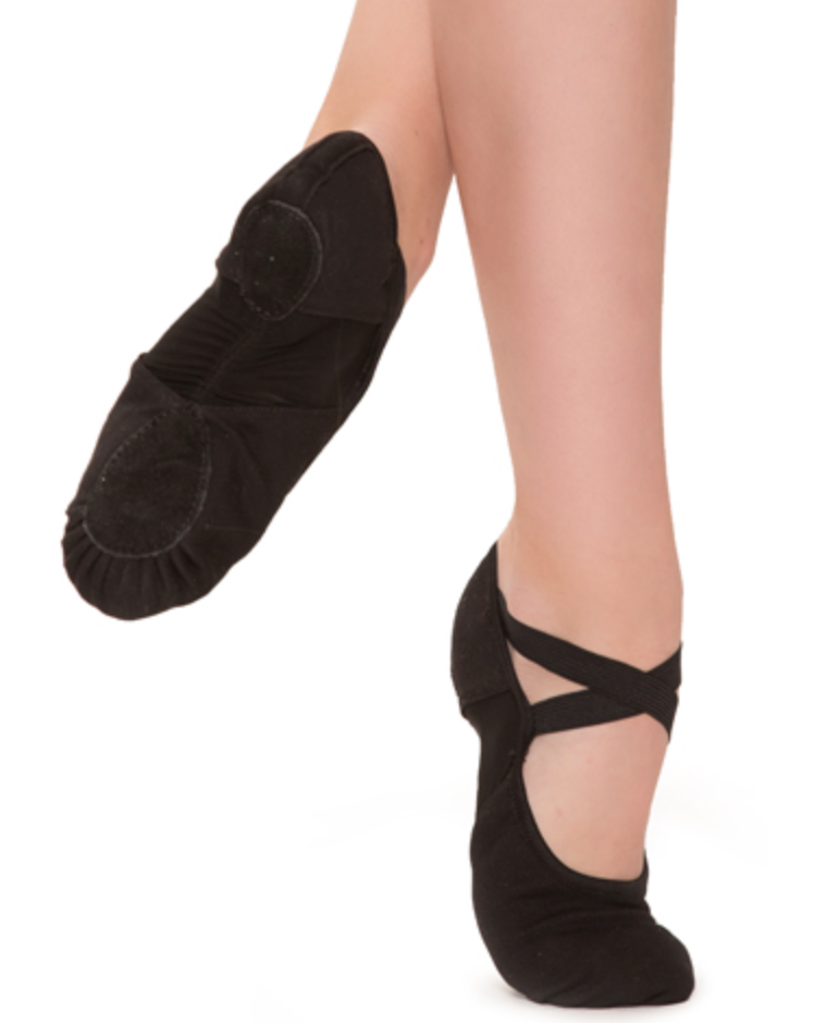 A studio shot of a dancer's lower legs and feet wearing black canvas split-sole dance shoes, one foot pointed with crossed elastic straps and the other flexed against a clean white background