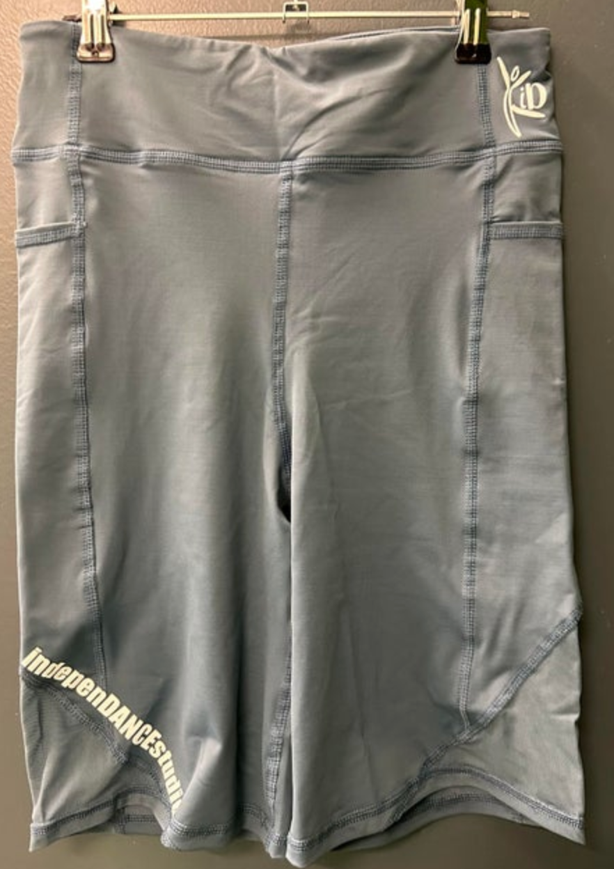 Photograph of dusty blue high-waisted athletic shorts with side pockets white IndepenDANCE Studio text on the lower left leg and a white stylized ID logo on the right waistband