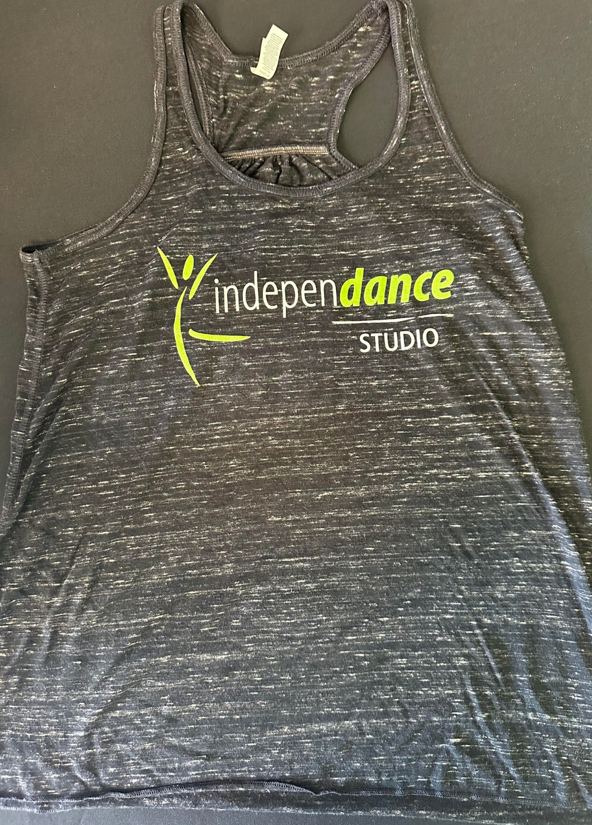 Photograph of a dark grey heathered racerback tank top featuring a bright lime green stylized figure and the "independance STUDIO" logo with "dance" in lime green lettering