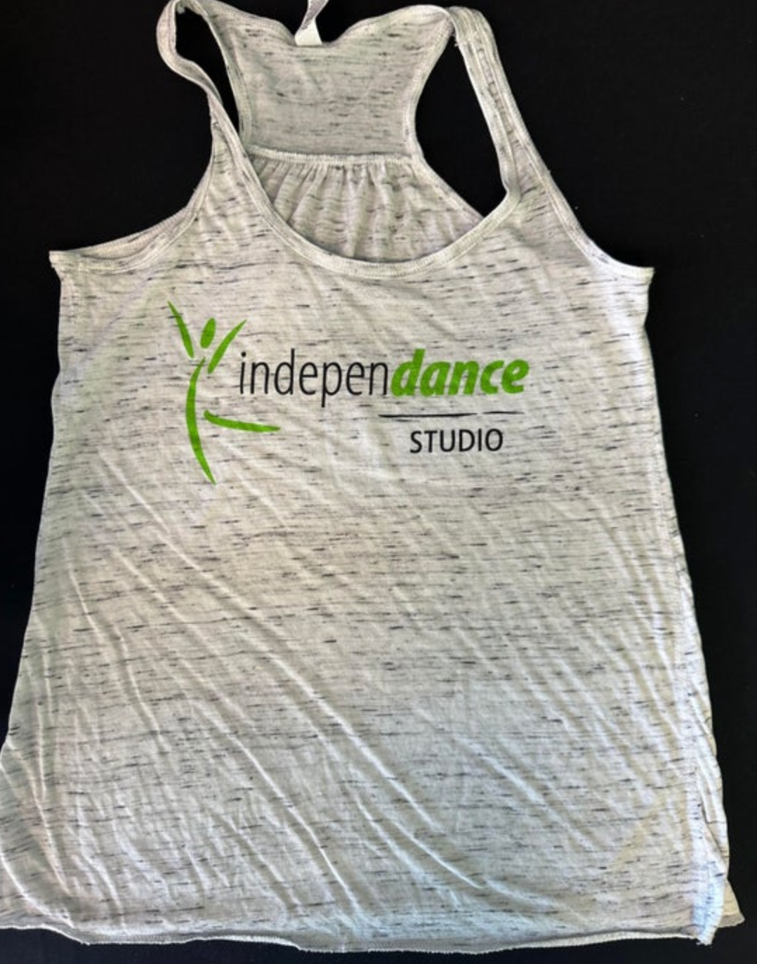 Photograph of a grey marled racerback tank top featuring the vibrant green stylized dancing figure logo and "indepen**dance** STUDIO" text with the "dance" part also in green
