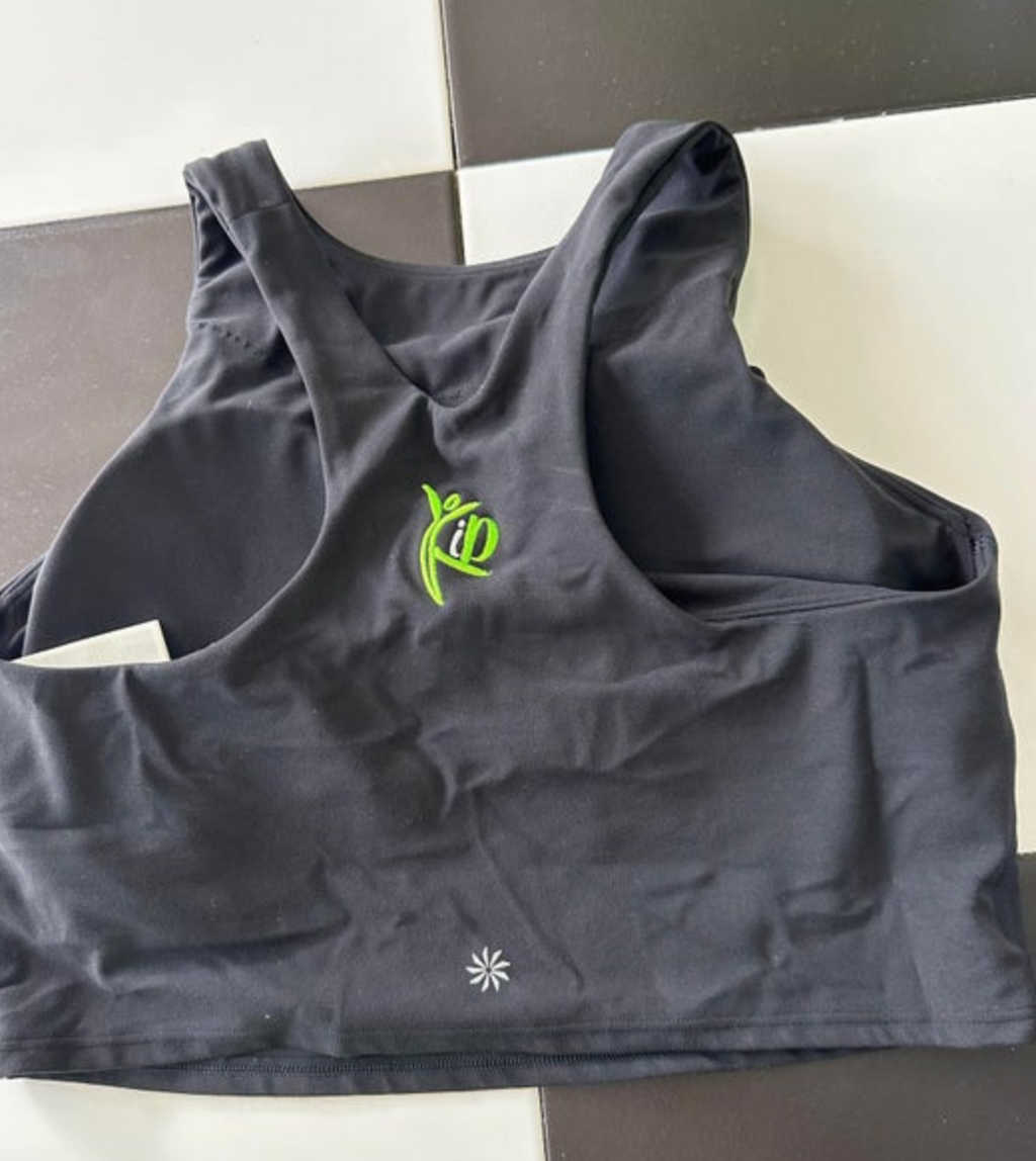 Photograph of a black Athleta athletic top featuring a bright green iP logo on the back and a white asterisk emblem near the hem, placed on a checkered black and white floor