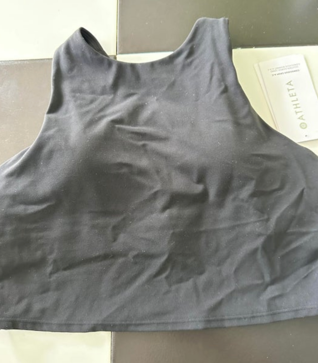Black Athleta high-neck athletic crop top with brand tag and visible fabric wrinkles on a two-tone tiled surface