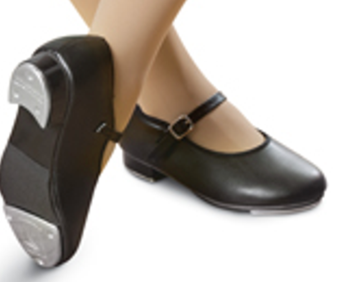 A close-up shot of a person's feet wearing black leather tap shoes featuring shiny silver taps on the heel and toe, secured by an ankle strap with a silver buckle on a plain white studio background