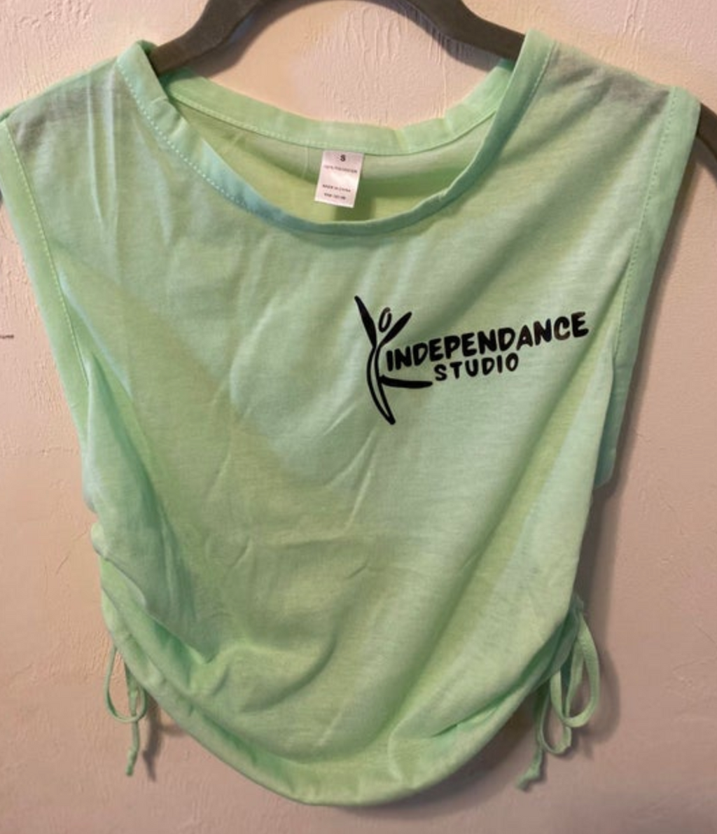 Photograph of a light green sleeveless tank top featuring a black INDEPENDANCE STUDIO dancer logo and adjustable ruched drawstrings on the sides