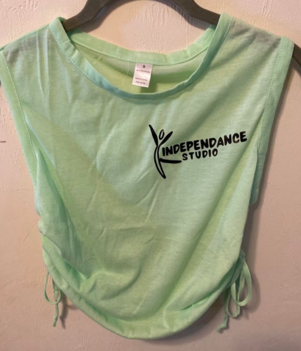 Photograph of a light green sleeveless tank top featuring a black INDEPENDANCE STUDIO dancer logo and adjustable ruched drawstrings on the sides