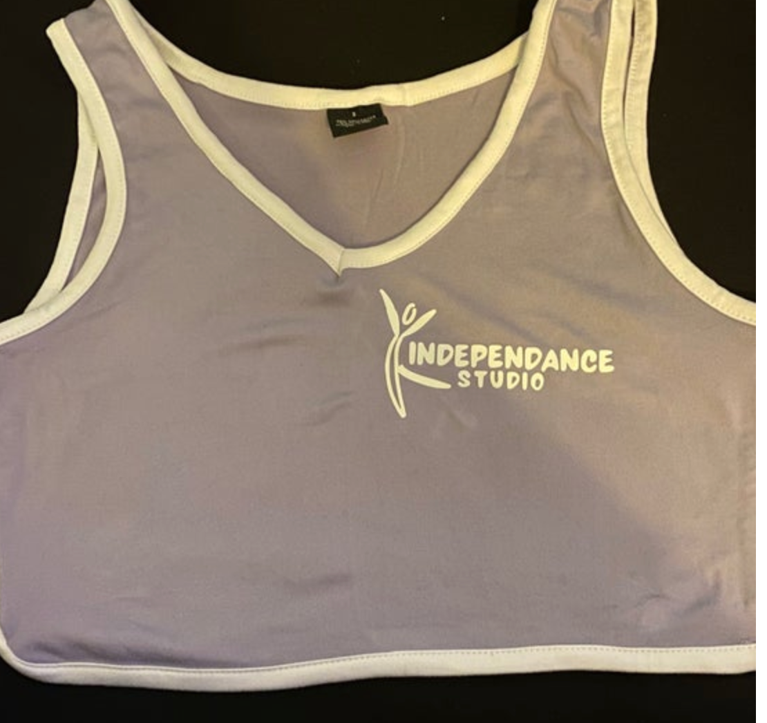 Lavender V-neck crop top featuring white trim along the neckline, armholes, and hem with a prominent white "INDEPENDANCE STUDIO" dancing figure logo on the chest