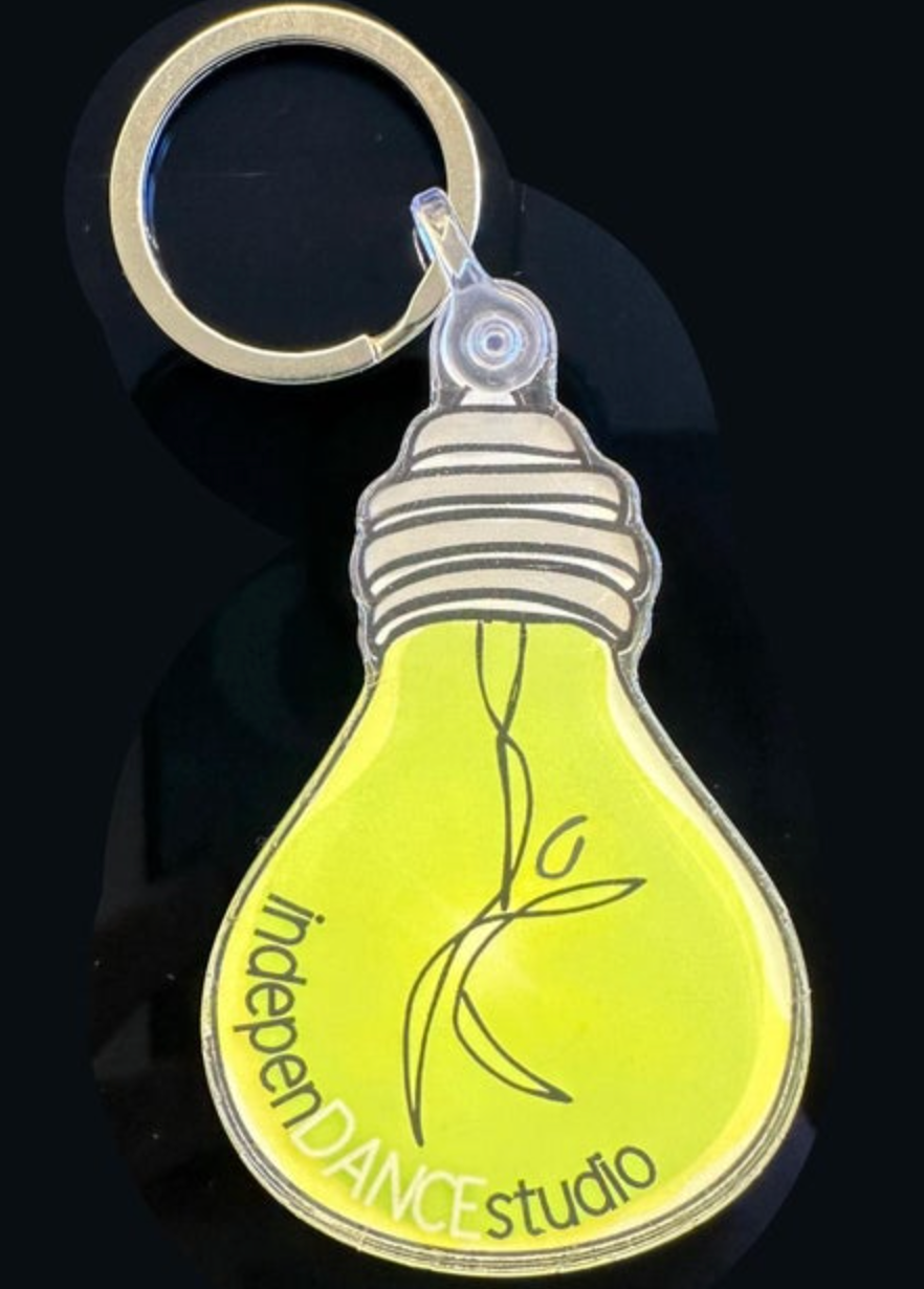 Keychain with a bright neon yellow lightbulb shape featuring the 'indepenDANCE studio' logo and a stylized dancing figure attached to a silver keyring