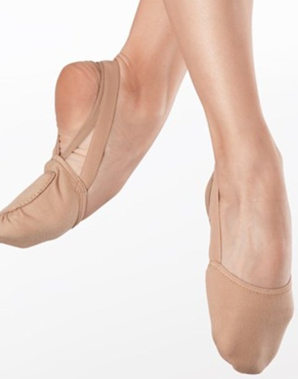 Close-up of a dancer's feet wearing nude tan split-sole ballet shoes with crisscross elastic straps posing on demi-pointe