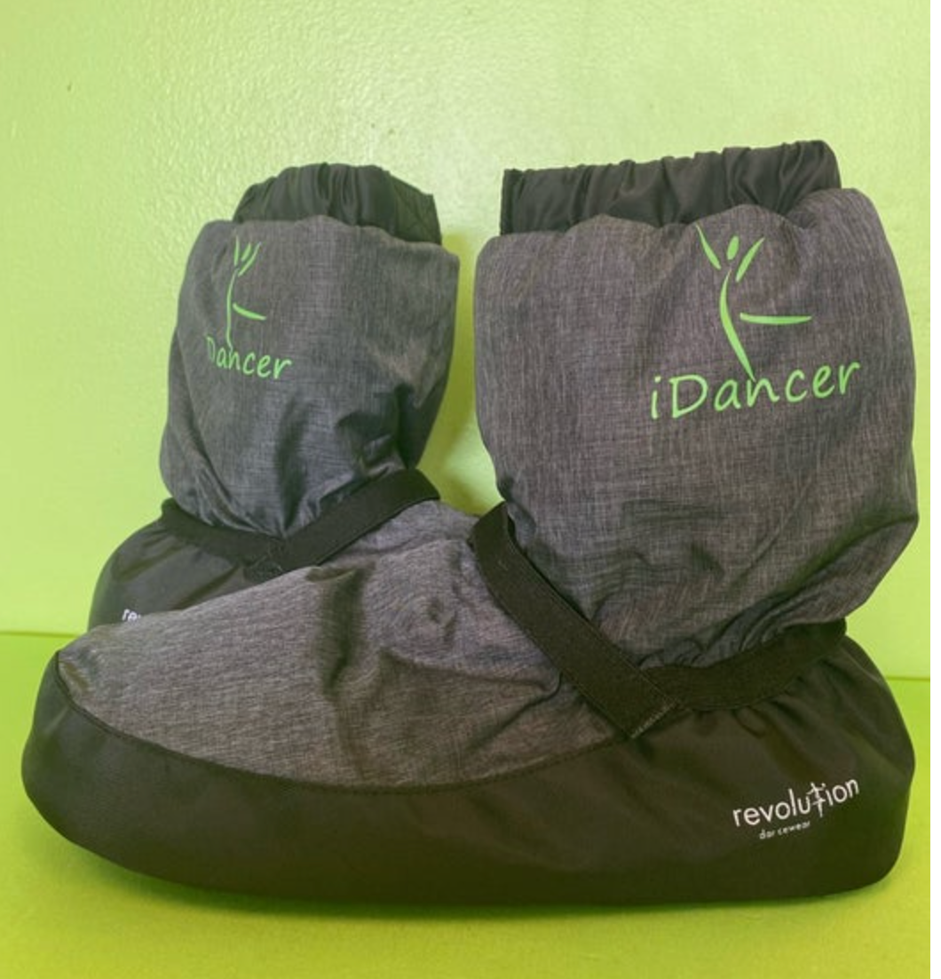 A pair of grey textured dance warm-up booties with black soles, featuring a fluorescent green iDancer logo with a dancer silhouette, black elastic straps and ruffled tops, and revolution dancewear text on a vibrant lime green background